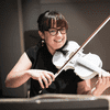 A woman smiling at the camera and playing a bright white violin.