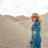 Margo Price walking in sand dunes in a blue jumpsuit and red sunglasses. 