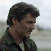 A closeup image of actor Pedro Pascal in the role of Joel from the HBO series, The Last of Us, looking down and to the side with a blurred background.