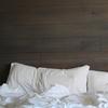 A white unmade bedspread with two white pillows against a wooden headboard