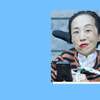A photo of Alice Wong, a Chinese American woman, against a blue background. She sits in a wheelchair and smiles. She has on a tiger striped sweater, red lipstick, and a tracheostomy tube is visible.