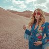 A photographed portrait of country singer, Margo Price, standing in a sandy desert scene, wearing big, red octagonal sunglasses, and a western-style blue suit with embroidered mushrooms. 