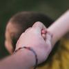 A close up photo of the back of child holding hands with an adult. 