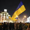 A Ukrainian flag is waved above a crowd at night 