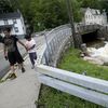 Pedestrians pass a local river whose heavy current flooded nearby Main Street, Monday, July 10, 2023, in Highland Falls, N.Y. Heavy rain has washed out roads and forced evacuations in the Northeast as