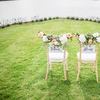 Two chairs on a green meadow facing a body of water. The backs of the chairs say 'forever' and 'always' and are adorned with floral wreaths. 