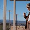 a man in a brown suit and brown fedora smoking a pipe in a desert like landscape.