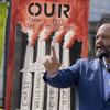 A photo of Sierra Club leader, Ben Jealous, wearing a blue suit and shirt and red pin that says, 'stop MVP' and he's speaking into a microphone at what looks like a climate protest.