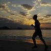A photo of a silhouetted figure jogging along a beach during sunset.