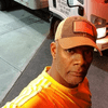 Adonis WIlliams, a Black man, takes a selfie in front of a truck. He's wearing an orange shirt and brown baseball hat.