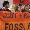 Protestors hold up an orange sign painted with flames. The words 'just+equitable fossil fuels' are visible 