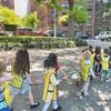 Children hold onto cords and wear yellow vests while they walk through a neighborhood with their daycare provider.