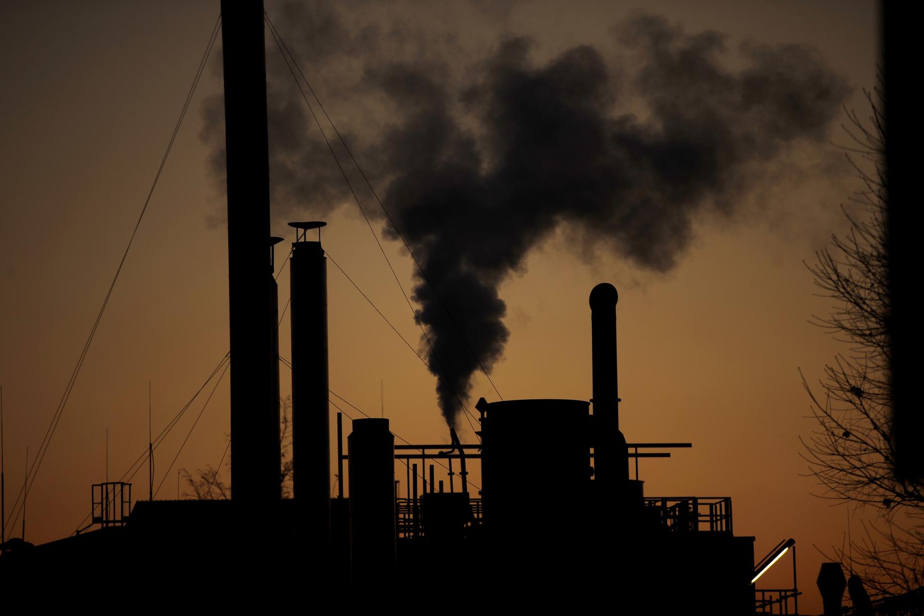 Silhouette of factory with smokestacks billowing smoke into a brownish-red sky