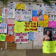 A demonstrator poses for a photo in front of a wall of signs against President-elect Donald Trump during a demonstration in downtown Los Angeles on Saturday, Nov. 12, 2016. 