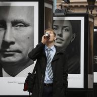 A man enjoys a drink as he walks past a portrait of Russian President Vladimir Putin displayed among portraits of Russian athletes, winners of the Sochi 2014 Winter Olympics at the photo exhibition.