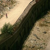 People walk past each other on opposite sides of the fence along the U.S. Mexican border