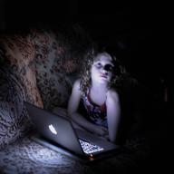 A young girl in a dark room takes a break from playing on the computer.