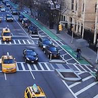 A protected bike lane separates cyclists from traffic with a line of parked cars or other barriers.