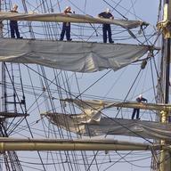 Crew members aboard the Danish merchant marine training ship, the Danmark, stand high above the deck on the rigging to unfurl the sails as the ship prepares to sail up the Chesapeake Bay.