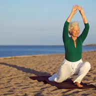 Senior woman practicing yoga poses on the sandy beach.