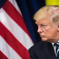 president donald trump leaning forward with flags in the background