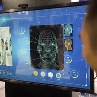 A man watches as a visitor tries out a facial recognition display at a booth for Chinese tech firm Ping'an Technology at the Global Mobile Internet Conference (GMIC) in Beijing, Thursday, April 26.