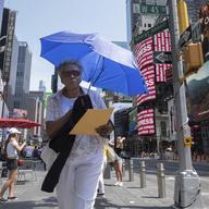 A woman uses an umbrella to block out the sun while walking through Times Square.