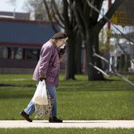A lone elderly woman carries her grocery bags up a hill and wipes her nose near downtown Aurora, Ill., Monday, April 20, 2020.