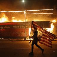 A protester carries a U.S. flag upside down, a sign of distress, next to a burning building Thursday, May 28, 2020, in Minneapolis. Protests over the death of George Floyd.
