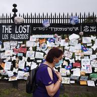 A woman passes a fence outside Brooklyn's Green-Wood Cemetery adorned with tributes to victims of COVID-19, Thursday, May 28, 2020, in New York.