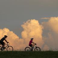 People ride bikes with cumulus clouds in the background, on the Mississippi River levee in Jefferson Parish, a suburb of New Orleans, Tuesday, July 14, 2020.