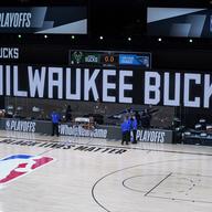 Officials stand beside an empty court at the scheduled start of an NBA basketball first round playoff game between the Milwaukee Bucks and the Orlando Magic, Wednesday, Aug. 26, 2020, in Florida.