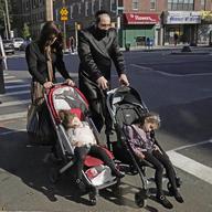 An ultra-Orthodox Jewish man and woman wheel strollers with sleeping children in them as they cross a street on the Jewish holiday of Sukkot, Sunday, Oct. 4, 2020, in Borough Park, Brooklyn.