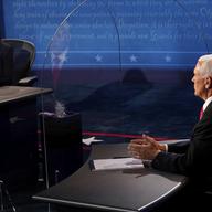 Democratic vice presidential candidate Kamala Harris, sitting at a black desk with a plexiglass divider, looks toward Vice President Mike Pence 