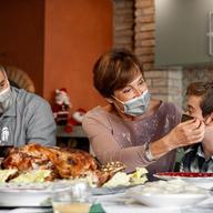 A family wears masks in front of a turkey at Thanksgiving.