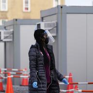 A worker wear a protective face shield walks between portable units set up for registration and testing at a New York City Health + Hospitals COVID-19 testing site in the Brooklyn borough of New York,