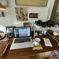 A home office desk cluttered with statues, photos and a wire shelf. 