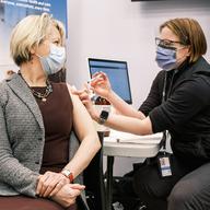 White woman giving another white woman a vaccination, both wearing masks