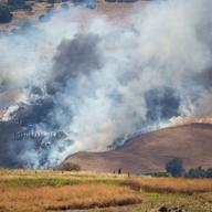 a wildfire covers dry golden hills in smoke and flames