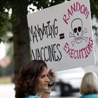 Woman holds sign which reads 'MANDATING VACCINE = RANDOM EXECUTIONS' with a skull and crossbones.