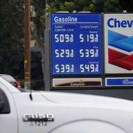 Blue chevron gas price board behind white pick up truck. Prices range from five dollars to $5.50.