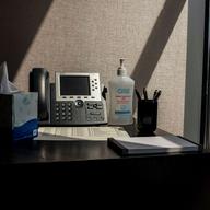 Light shines on a desk with a landline phone, pens, and a bottle of hand sanitizer.