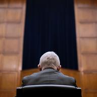 Anthony Fauci is seen from behind sitting in a seat of a courtroom.