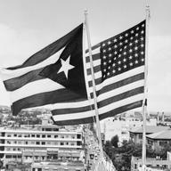 A Puerto Rican flag and a U.S. flag fly above San Juan. 