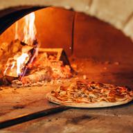 two pizzas in a traditional pizza oven with fire burning behind it
