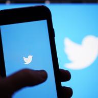 A hand holds up a phone screen featuring the twitter logo.