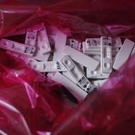 A closeup image looking inside a red translucent medical bag containing a messy pile of discarded rapid diagnostic test cards for COVID-19. 