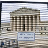 A black fence is in the foreground, the Supreme Court in the background. On the fence a sign reads 'area closed'