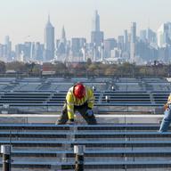 Framed by the Manhattan skyline, electricians with IBEW Local 3 install solar panels on top of the Terminal B garage at LaGuardia Airport, Nov. 9, 2021, in the Queens borough of New York.