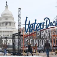 With the U.S. Capitol in the background, people walk past a sign that says say, 'Voters Decide Protect Democracy,' Jan. 6, 2022, in Washington.